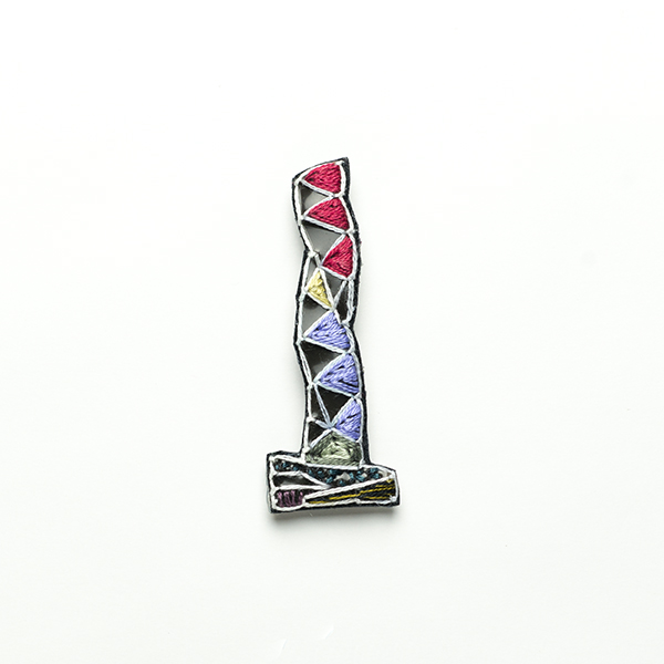 B35 タワーブローチ〈柘榴(ざくろ)/藤色×白〉<br>制作者:Kimiko Sekine<br>サイズ:7cm×2.5cm<br>素材:布、PPシート、フェルト、刺繍糸、ブローチピン<br><br>水戸芸術館のタワーはいつも変わらず佇んでいますが、いつも違ってみえます。このブローチはガーネットの輝きに照らし出されるタワーをイメージして作りました。