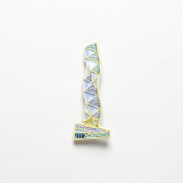 B36 タワーブローチ〈アルティメットグレー×イエロー〉<br>制作者:Kimiko Sekine<br>サイズ:7cm×2.5cm<br>素材:布、PPシート、フェルト、刺繍糸、ブローチピン<br><br>水戸芸術館のタワーはいつも変わらず佇んでいますが、いつも違ってみえます。このブローチは日が昇り力強くのびのびとたたずむタワーをイメージして作りました。