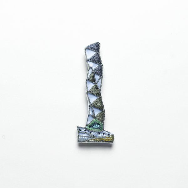 B37 タワーブローチ〈グラファイト〉<br> 制作者:Kimiko Sekine<br>サイズ:7cm×2.5cm<br>素材:布、PPシート、フェルト、刺繍糸、ブローチピン<br><br>水戸芸術館のタワーはいつも変わらず佇んでいますが、いつも違ってみえます。このブローチは千波湖のほとりから望む水戸芸術館のタワーをイメージして作りました。