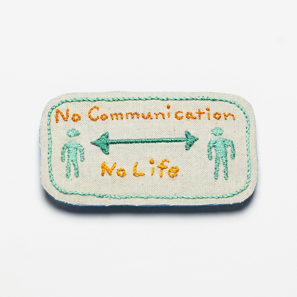 B24 No Communication No Life<br>制作者:わたげ<br>サイズ:4.3cm×7.6cm<br>素材:刺繍糸、布、フェルト、ブローチピン<br><br>劇場勤務でも使うようになった「ソーシャルディスタンス」のサイン。 それでも私たちのコミュニケーションは止められない。