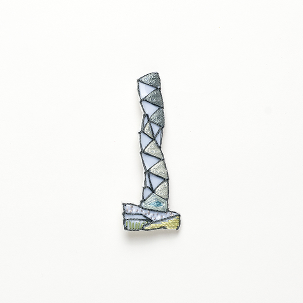 B75 タワーブローチ〈スカイグレー/シルバー×ダークグレー〉<br>制作者:Kimiko Sekine<br>サイズ:7cm×2.5cm<br>素材:布、PPシート、フェルト、刺繍糸、ブローチピン<br><br>水戸芸術館のタワーはいつも変わらず佇んでいますが、いつも違ってみえます。このブローチは、らせんの動きのように、四季を巡りながら時を重ねるタワーをイメージして作りました。