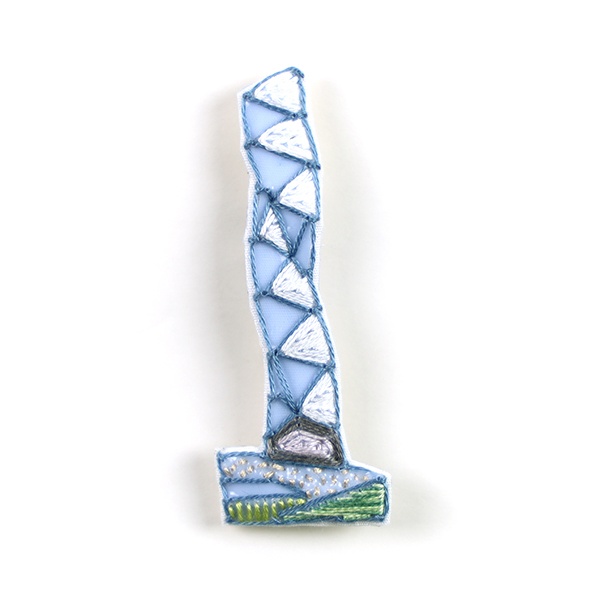 B158 タワーブローチ〈ホワイト/スノーホワイト×ブルー〉<br>制作者:Kimiko Sekine<br>サイズ:7cm×2.5cm<br>素材:布、PPシート、フェルト、刺繍糸、ブローチピン<br><br>水戸芸術館のタワーはいつも変わらず佇んでいますが、いつも違ってみえます。このブローチは雪晴れの広場を映し込んだタワーをイメージして作りました。