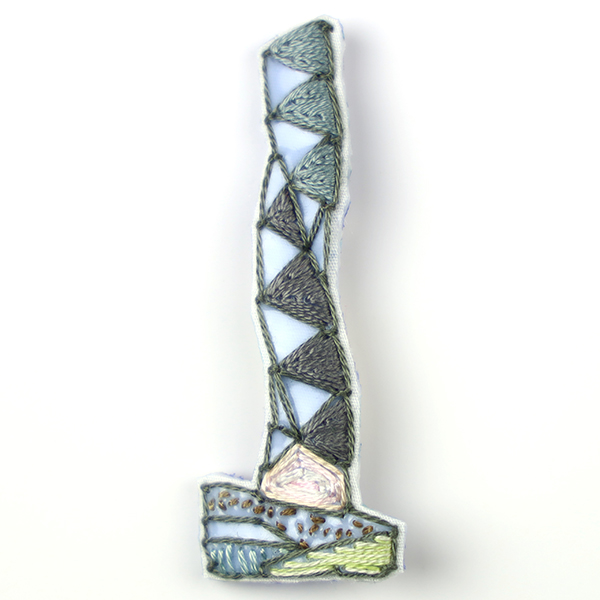 B256 タワーブローチ〈ブルーグレー/スモークグレー×ミディアムグレー〉<br>制作者:Kimiko Sekine<br>サイズ:7cm×2.5cm<br>素材:布、PPシート、フェルト、刺繍糸、ブローチピン<br><br>水戸芸術館のタワーはいつも変わらず佇んでいますが、いつも違ってみえます。このブローチは、向春の日差しで温む広場に静かに佇むタワーをイメージして作りました。