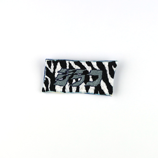 B644 ジラフ?<br>制作者:わたげ<br>サイズ:2.8cm×6cm<br>素材:フェルト、布、刺繍糸、ブローチピン<br><br>中﨑透さんの展覧会で、文字情報と視覚情報の伝達について考えさせられました。それらのちぐはぐさのおもしろ味を、私もブローチという小さな世界に落とし込みたいと思いました。