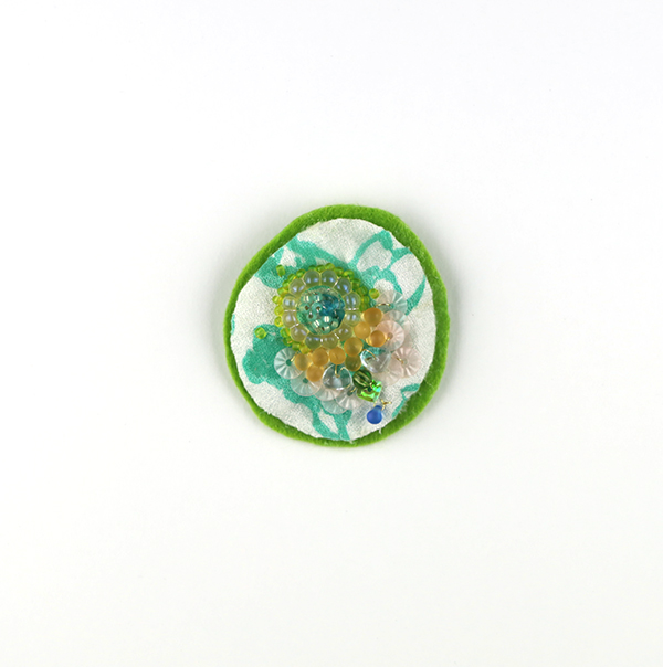 B657 風にまう<br>制作者:Ki<br>サイズ:4.2cm×4.5cm<br>素材:布、刺繍糸、フェルト、金糸、ビーズ、スパンコール、ブローチピン<br><br>遠くから見た花をイメージしたブローチです。