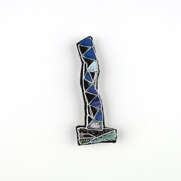 B695 タワーブローチ〈蒼玉×明灰色〉<br>制作者:Kimiko Sekine<br>サイズ:7cm×2.5cm<br>素材:布、PPシート、フェルト、刺繍糸、ブローチピン<br><br>水戸芸術館のタワーはいつも変わらず佇んでいますが、いつも違ってみえます。このブローチは、ライトアップされたArt Tower Mitoのシンボルタワーをイメージして作りました。