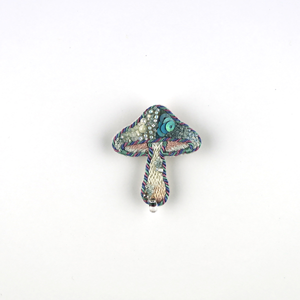 B699 土に還る‶鱗(青)“<br>制作者:itoco<br>サイズ:4cm×3.5cm<br>素材: フェルト、刺繍糸、組紐、レース糸、ビーズ、淡水パール、合成皮革、ブローチピン<br><br>うろこが生えてしまったキノコ。石づきにも小さなうろこが生え始め…