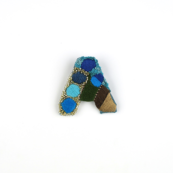 B763 アルファベット -A-<br>制作者:Sukesan<br>サイズ:4cm×4cm<br>素材:刺繍糸、ビーズ、フェルト、布、合皮、ブローチピン<br><br>そのアルファベットからはじまるストーリーが、すてきなものでありますように。